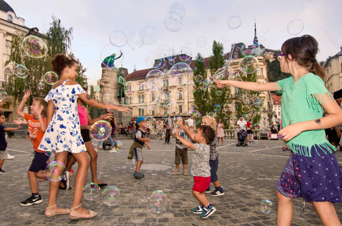 Children of different age are catching bubbles in the city square.