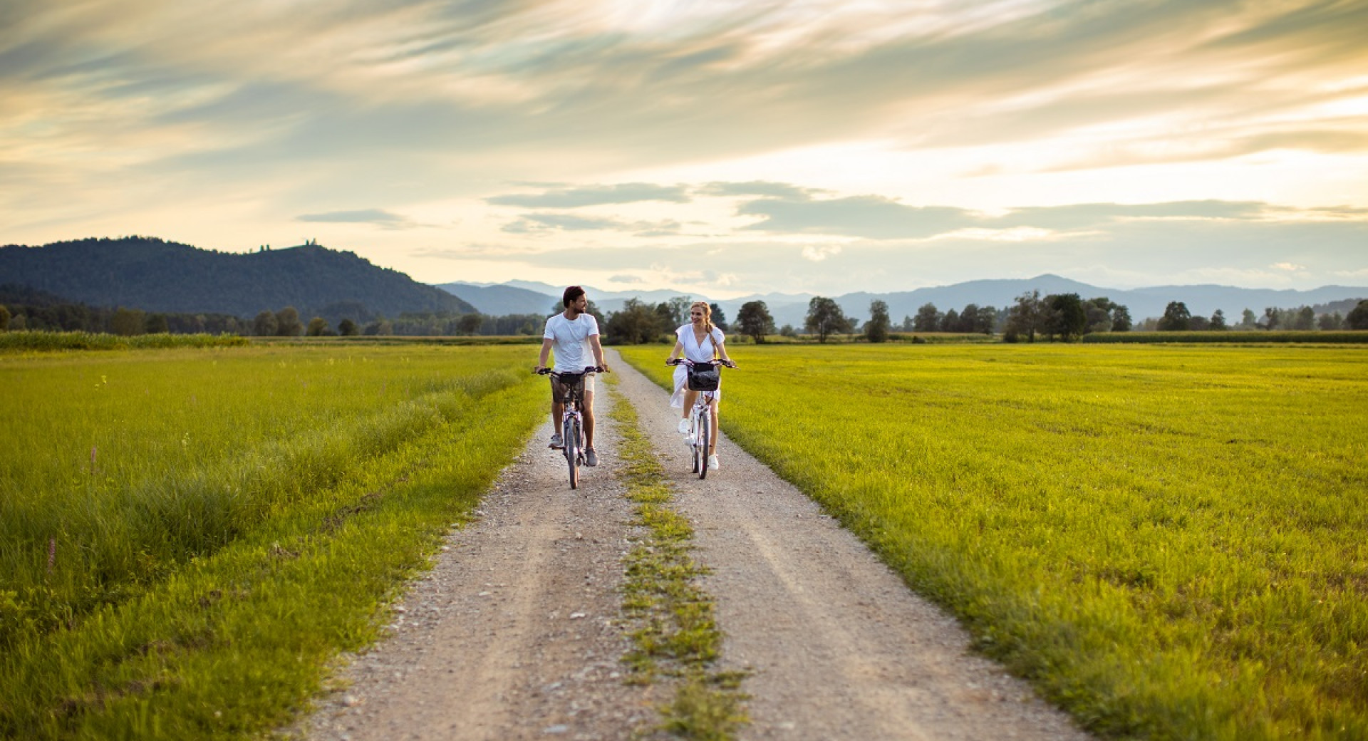 Two people cycling on an unpaved road with a green surroundings.