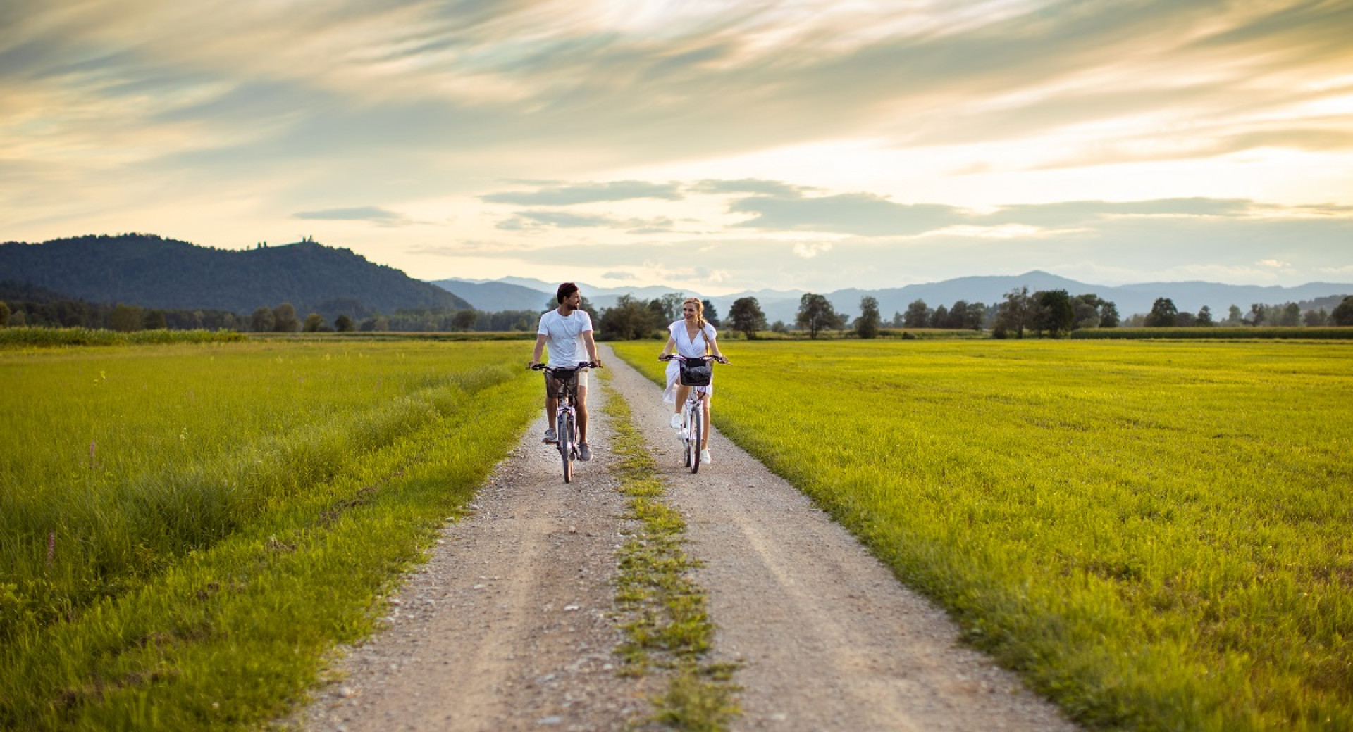 Two people cycling on an unpaved road with a green surroundings.