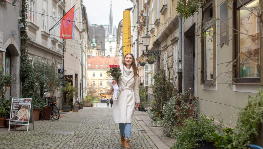 A young woman with a bouquet of roses walking in a beautiful alley.