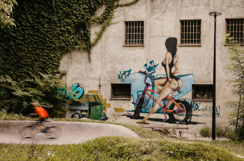 Grafit zapeljive zenske na kolesu. Stara stavba, obrasla z brsljanom.