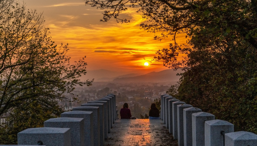 Par sedi na koncu dolgega prehoda z betonskimi stebri na obeh straneh. Uzivata v soncnem zahodu nad mestom.