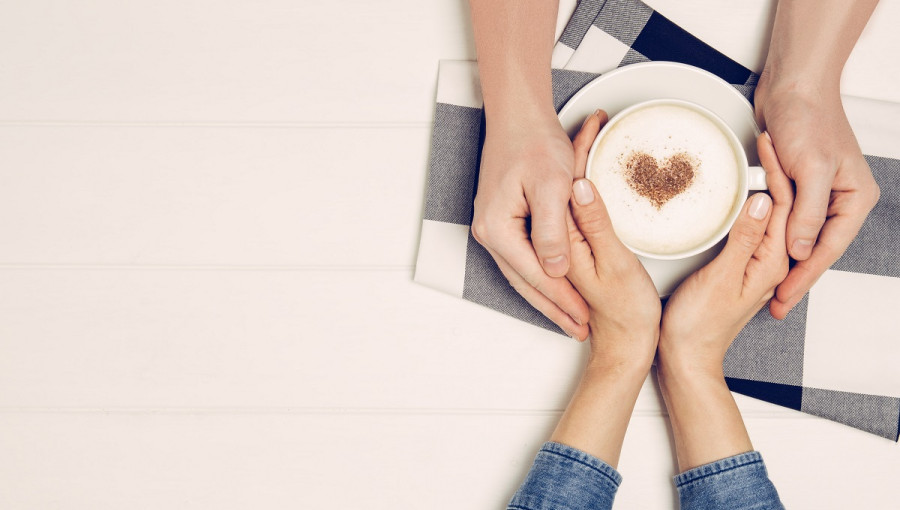 Roke dveh zaljubljencev objemajo kavo s srcem.