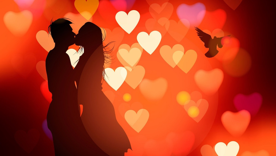 A silhouette of a kissing couple. Numerous hearts in the background.
