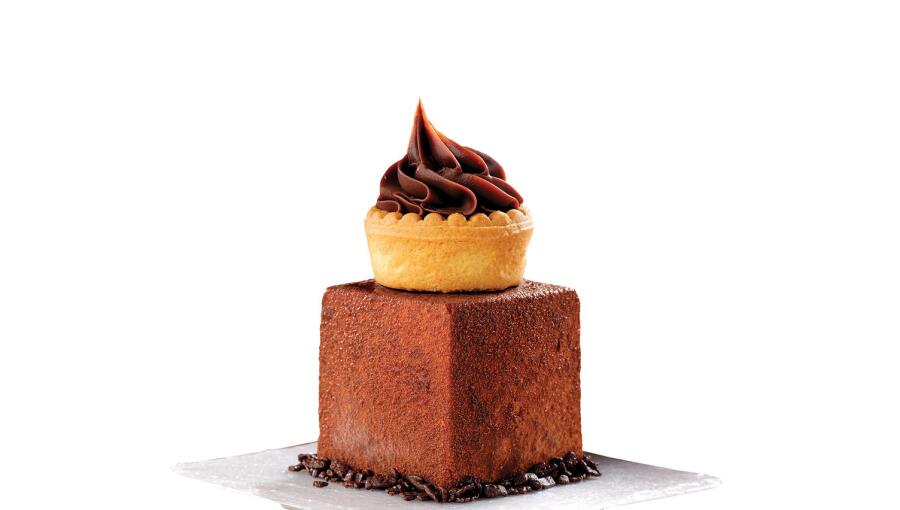 On the plate sits a chocolate cake topped with a small pastry covered in rich chocolate cream.