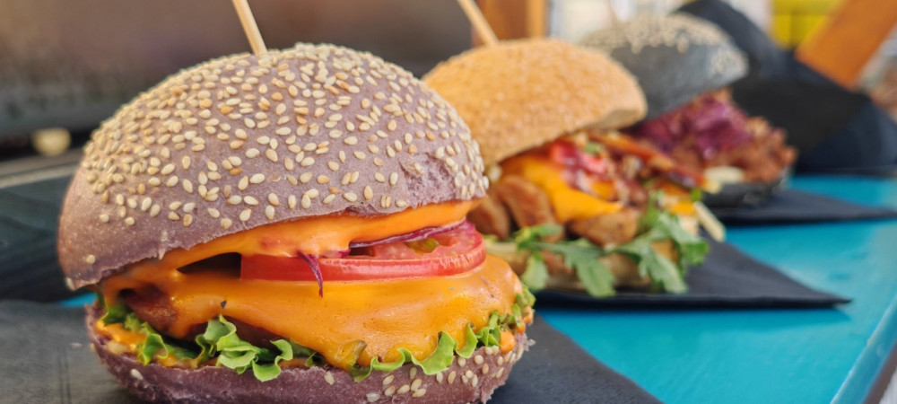 Mamljivi veganski burgerji na crnem prticku, razpostavljeni na modri mizi.