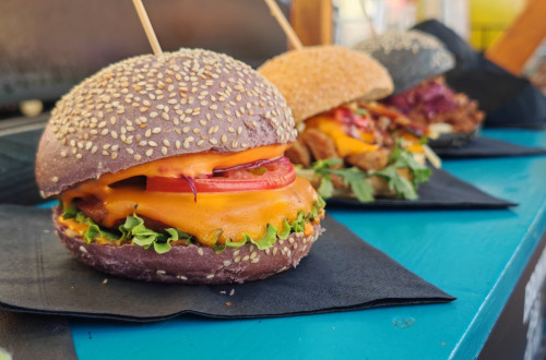 Mamljivi veganski burgerji na crnem prticku, razpostavljeni na modri mizi.