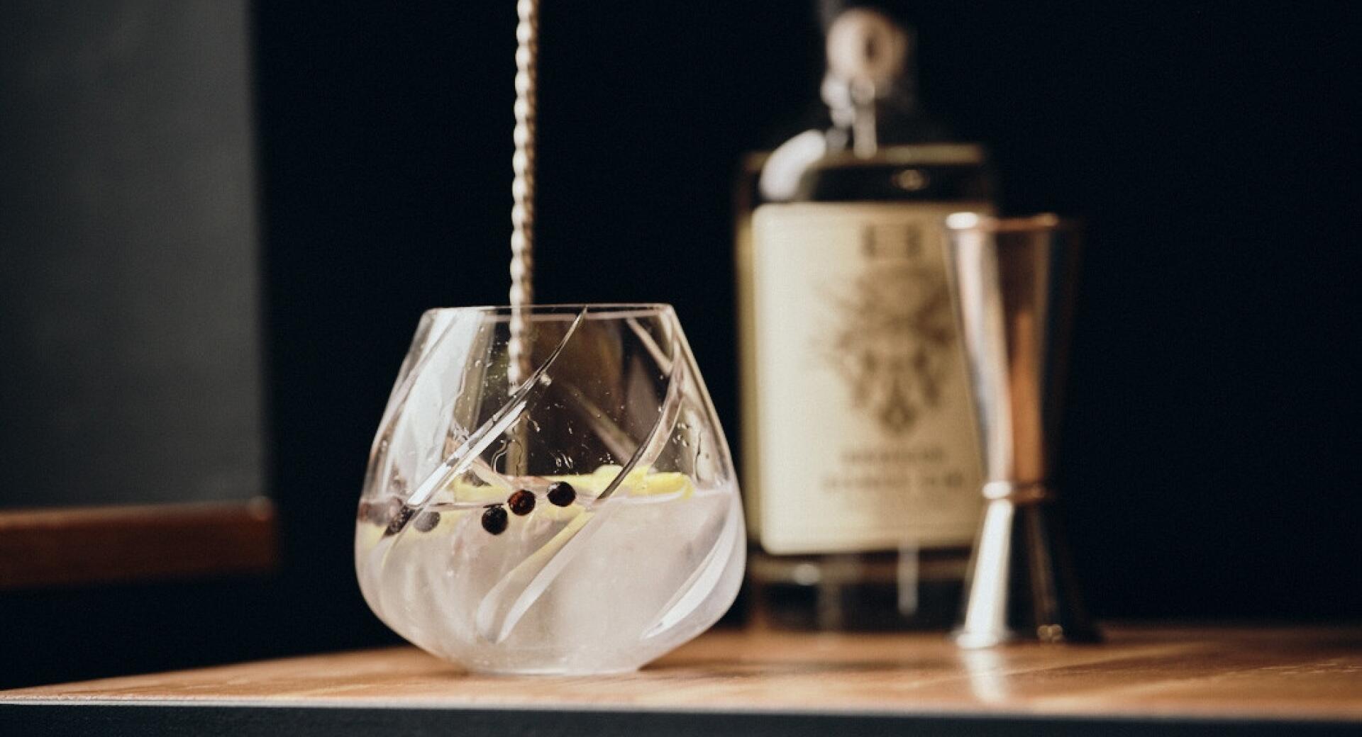Gin v kozarcu na mizi, v ozadju steklenica.