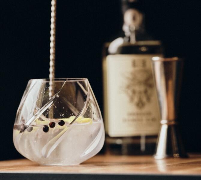 Gin in un bicchiere sul tavolo, con una bottiglia sullo sfondo.