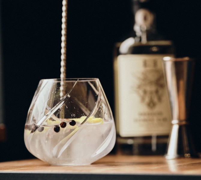 Gin in a glass on the table, with a bottle in the background.