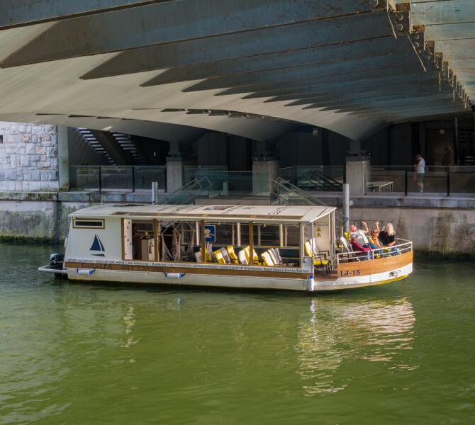 The tourist boat Barka Lea carrying passengers cruises on the green Ljubljanica River directly beneath the Butchers' Bridge.
