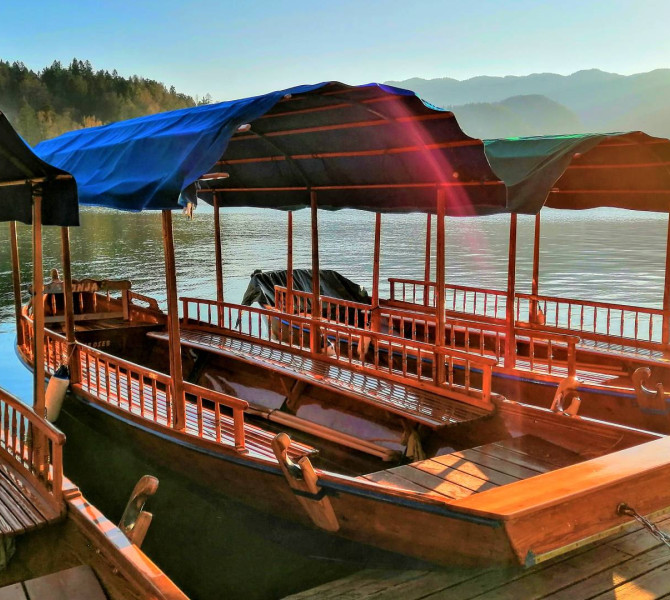 Holzboote mit Dächern, die bei Sonnenuntergang am Steg eines ruhigen Sees vertäut sind.
