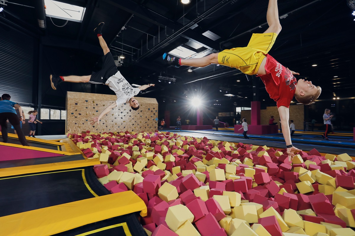 Men jumping into a pool filled with soft foam cubes.