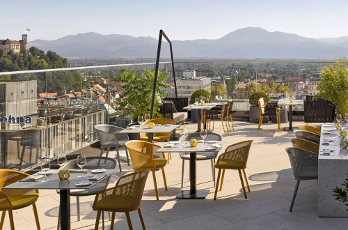 Zunanja terasa hotela s pogrnjenimi mizami in pogledom na Ljubljanski grad. 