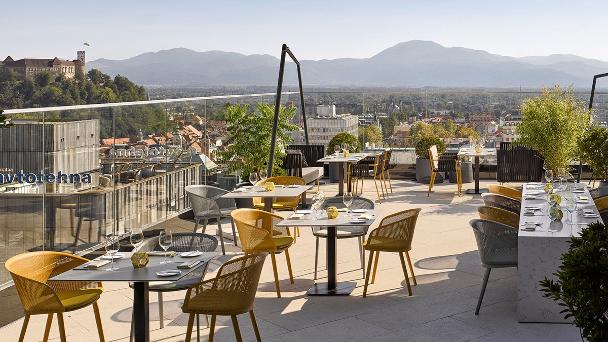 Zunanja terasa hotela s pogrnjenimi mizami in pogledom na Ljubljanski grad. 