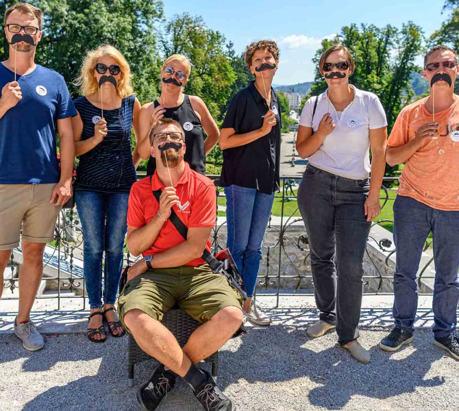 Obiskovalci ogleda na skupinski sliki z umetnimi brki na palcki.