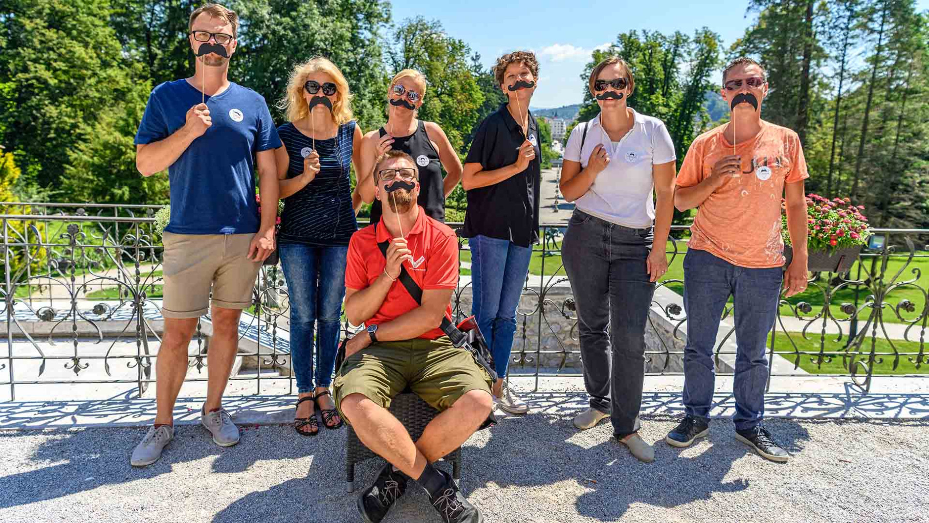 Obiskovalci ogleda na skupinski sliki z umetnimi brki na palčki.