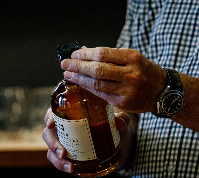 A man’s hand wearing a watch opening a whisky bottle.