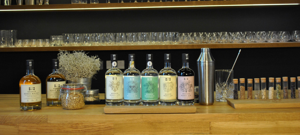 Five bottles on a wooden base. Glasses in the background.
