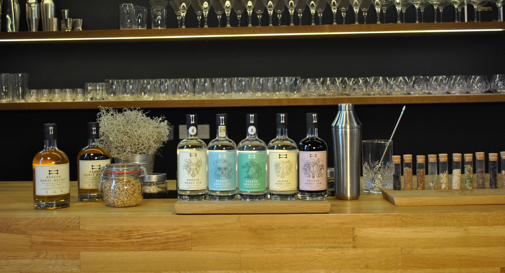 Five bottles on a wooden base. Glasses in the background.