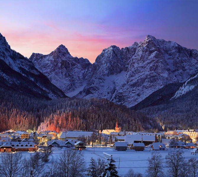 Mesto pod gorami v snegu in sončnem zahodu.
