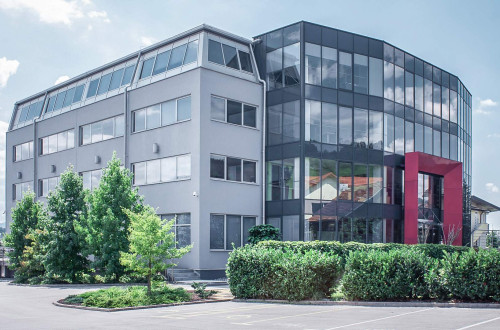 A large gray building with large windows and a red entrance to the building.