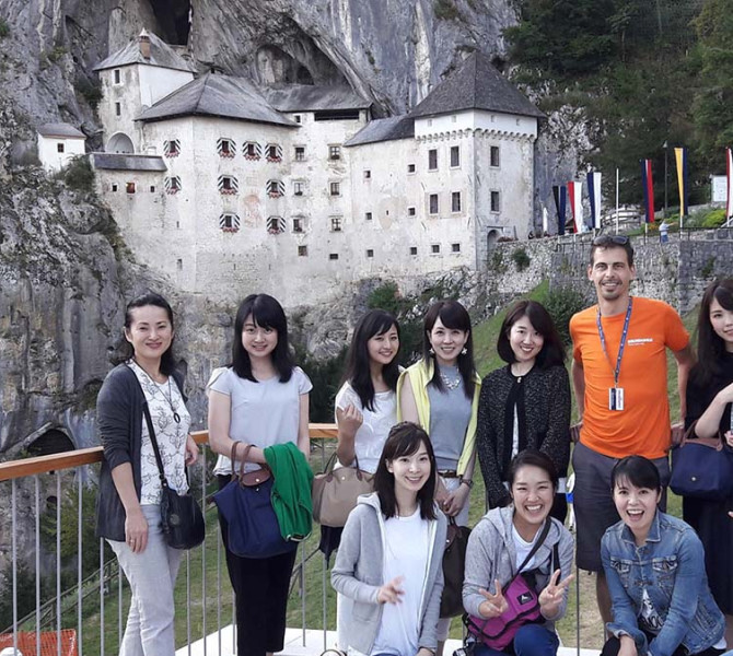 A group of people and a guide on the bridge. Predjama Castle in the background.