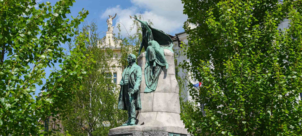 A monument to the greatest Slovenian poet France Prešern, above him is a muse, surrounded by trees.