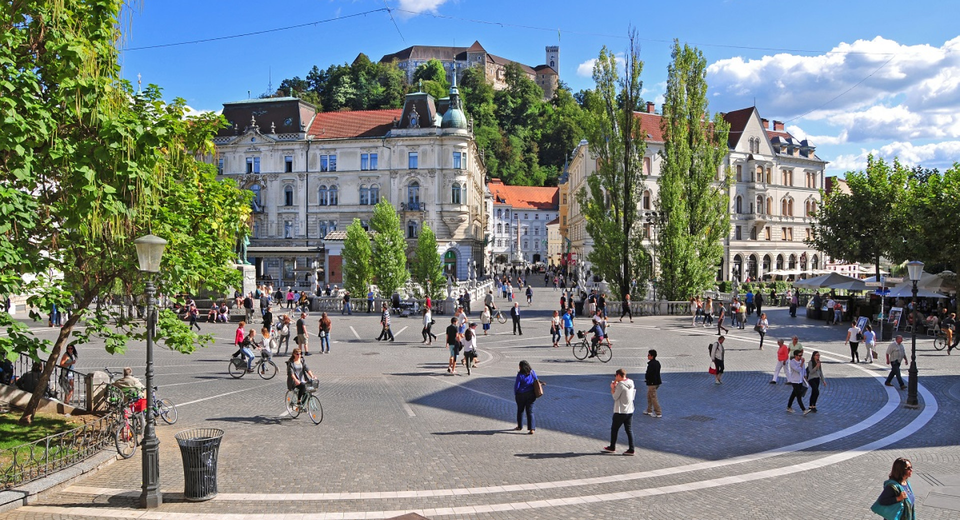 People walking in the city square with trees all around.