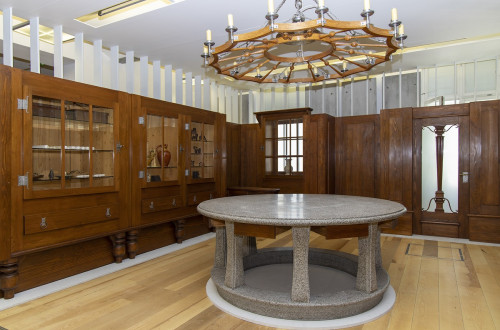 A room with wooden walls. A big wooden chandelier with candles in the middle.