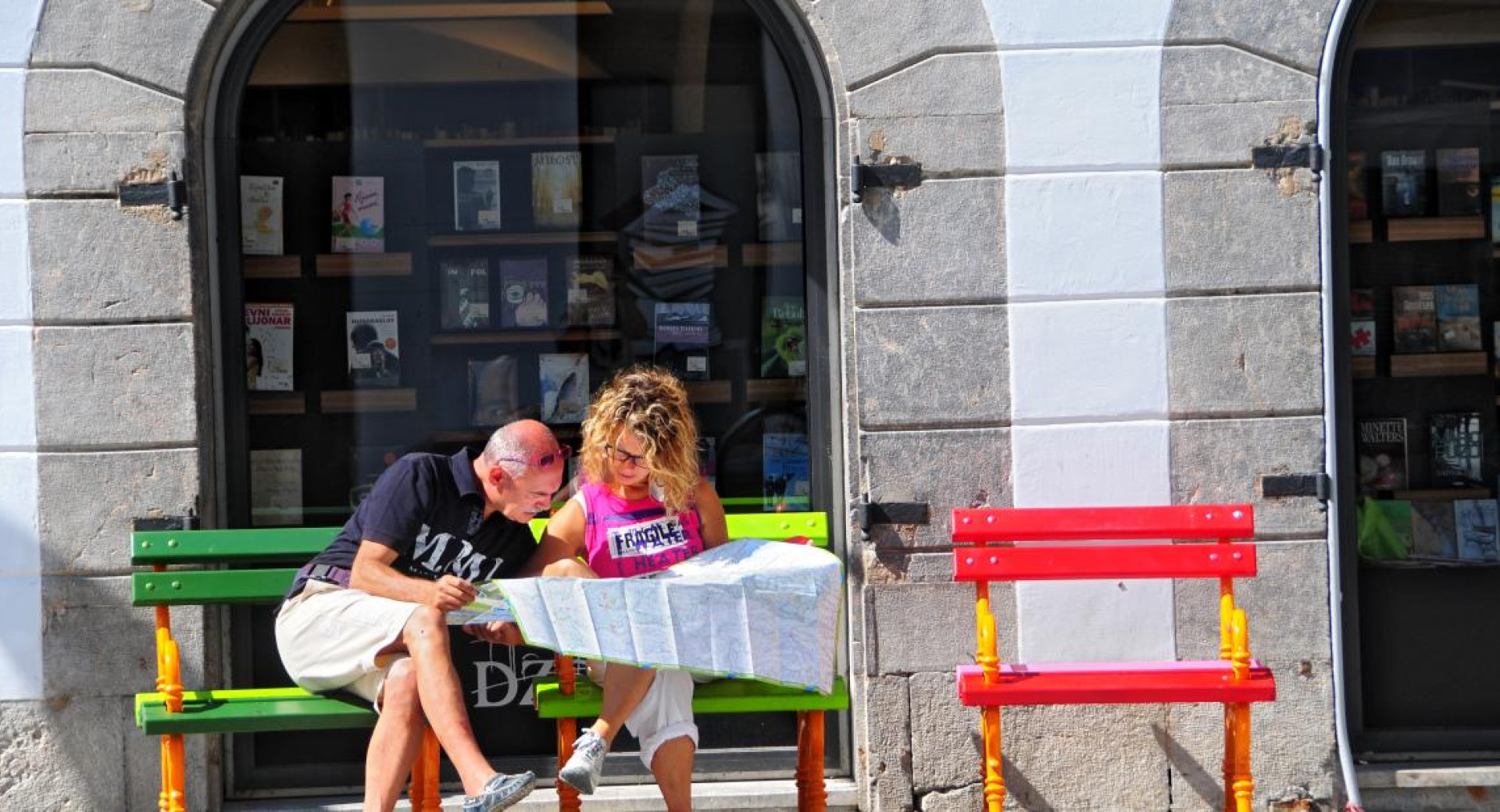 Dva turista gledata zemljevid in sedita na klopci v centru Ljubljane.