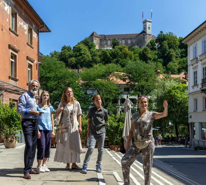 A family on a guided tour of Ljubljana, with Ljubljana Castle in the background.