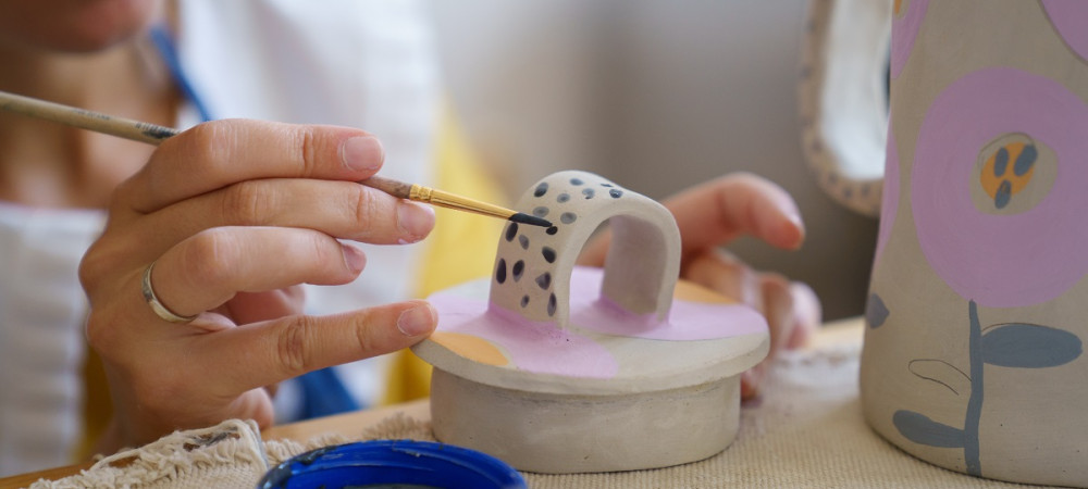 Zenska s copicem rise temne pikice po beli glineni umetnini.