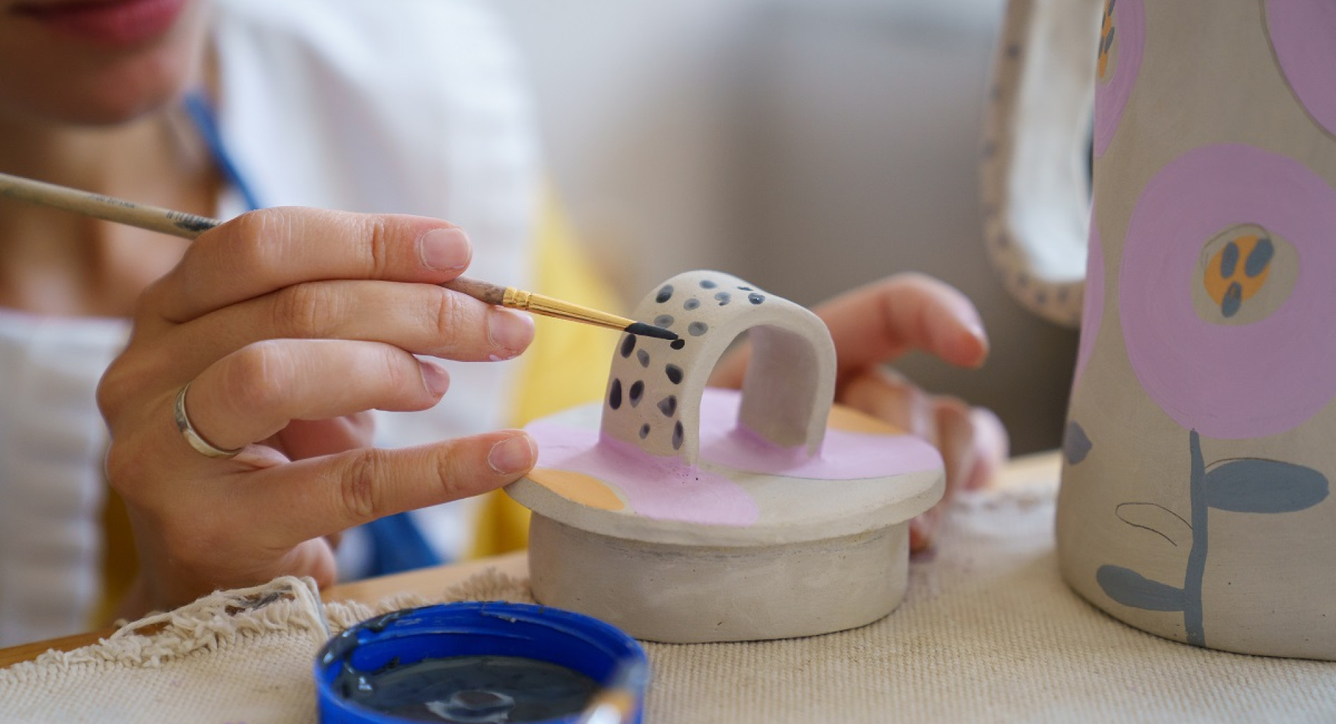 A woman using a brush to paint dark spots on a white clay art.