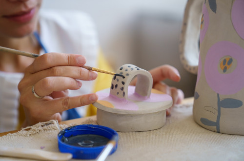 A woman using a brush to paint dark spots on a white clay art.