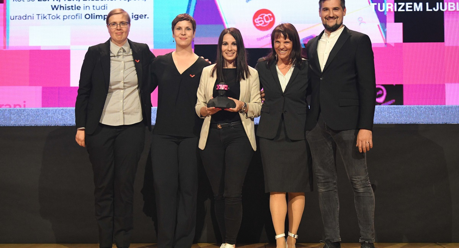 Four women and a man holding an award on stage.