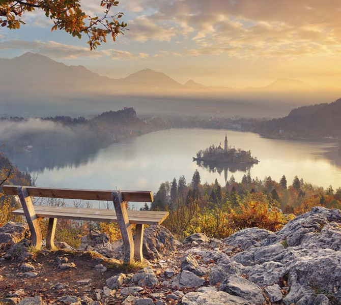 Una panchina su una roccia con vista su un isolotto in mezzo al lago. Colori autunnali.