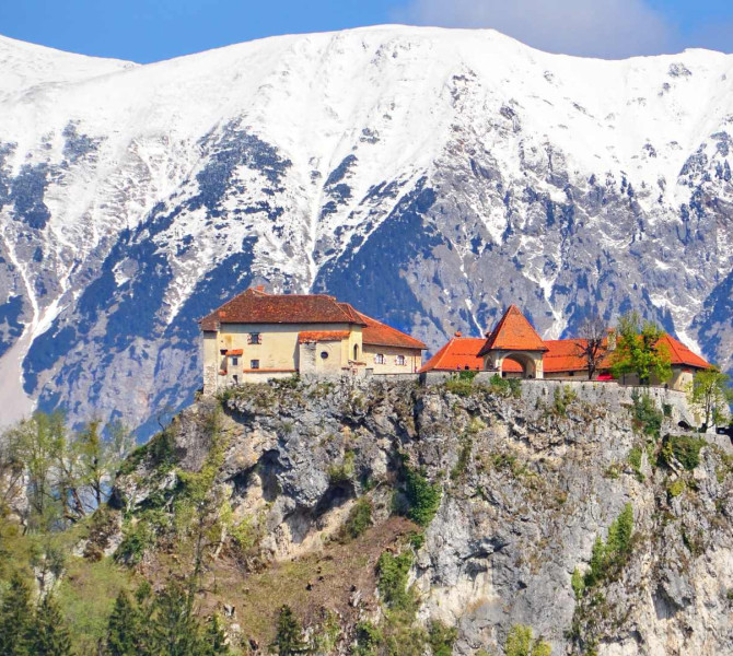 Castle on a steep rock, with snow-capped mountains in the background.