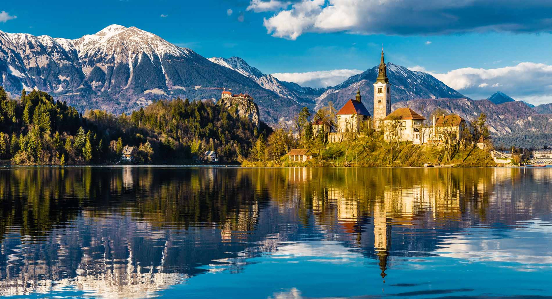 Blejsko jezero in otok sredi jezera s cerkvijo na vrhu, v ozadju pa se dvigajo zasnezene gore.