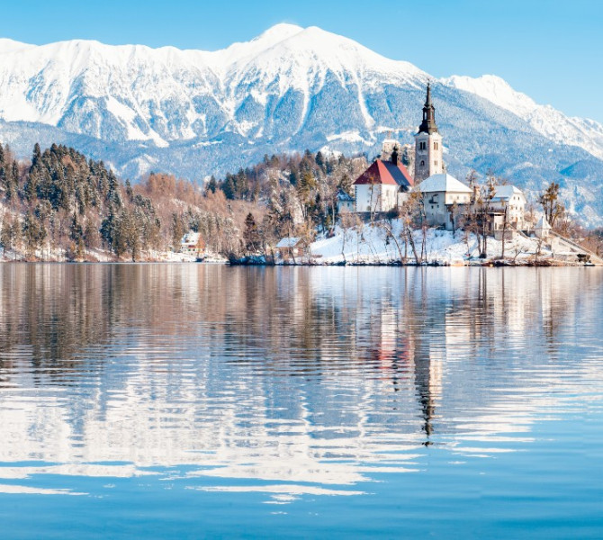 Otoček sredi jezera, na njem cerkvica v snegu. V ozadju gore.