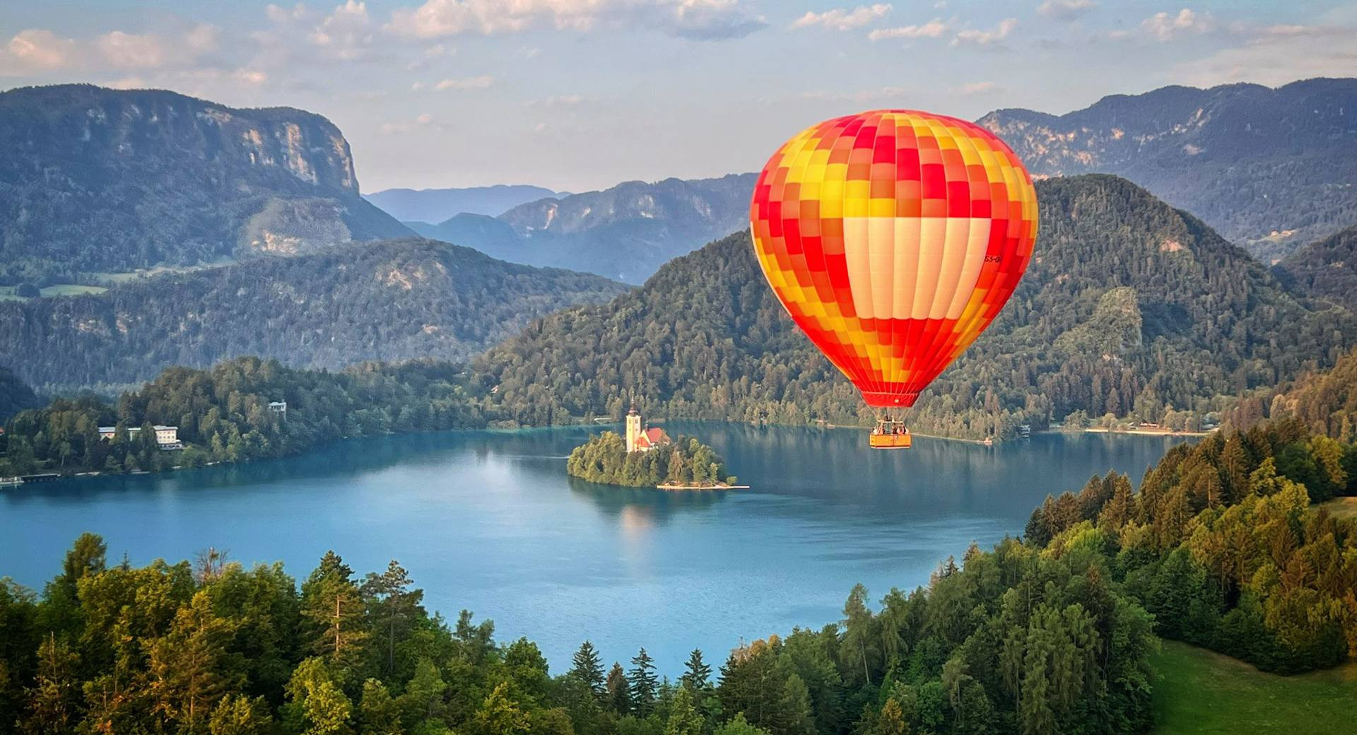 Un volo con una mongolfiera gialla e rossa sopra il lago di Bled.