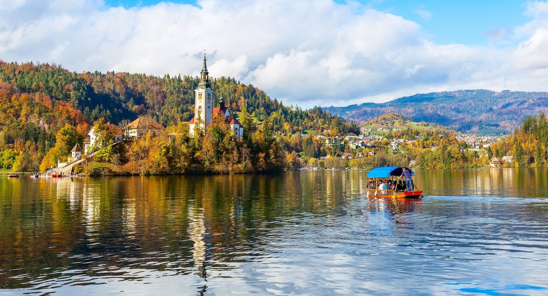 Una barca di legno sul lago naviga verso l'isolotto con la chiesetta. Colori autunnali.