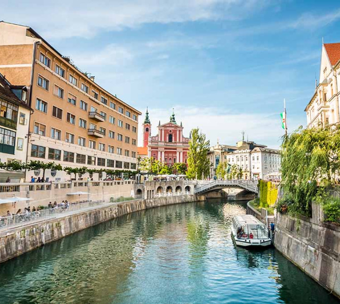 View from the bridge of the Ljubljanica River and a boat. On both sides of the river are the riverbanks.