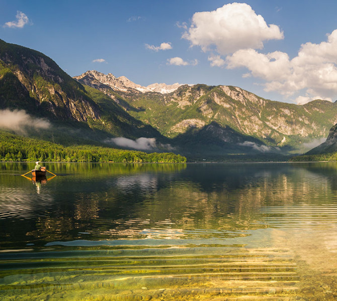 A boat in the middle of the lake in the morning mist, with mountains in the background.