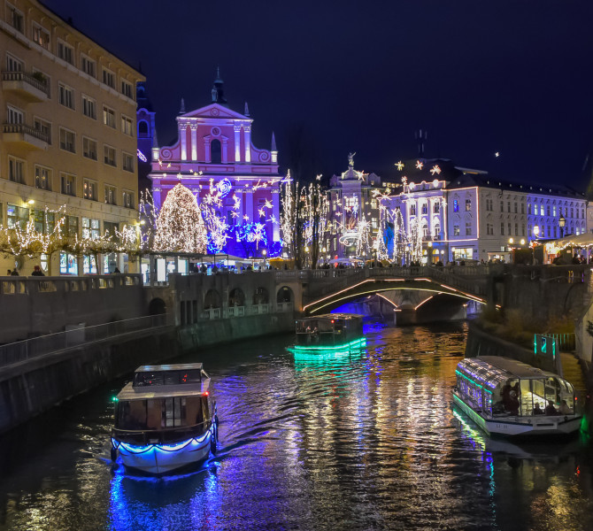 Colni na reki, stavbe in drevesa, okraseni s praznicnimi lucmi, ki zvecer zazarijo v pisanih barvah.
