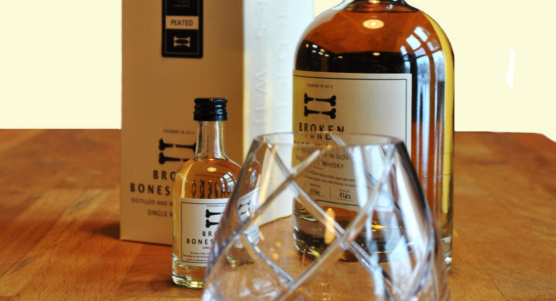 A bottle of whisky on a wooden table, with a glass beside it.