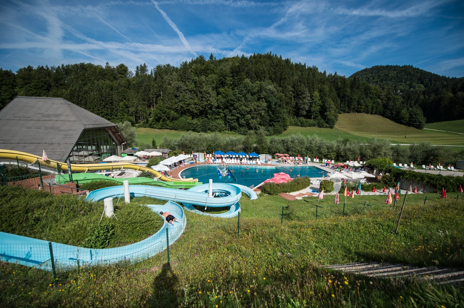 A waterslide and an outdoor pool. The surrounding area consists of forest and meadows.