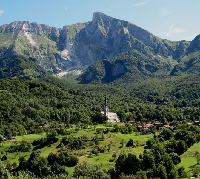 A small church on a hill surrounded by forest. Mountains in the background.