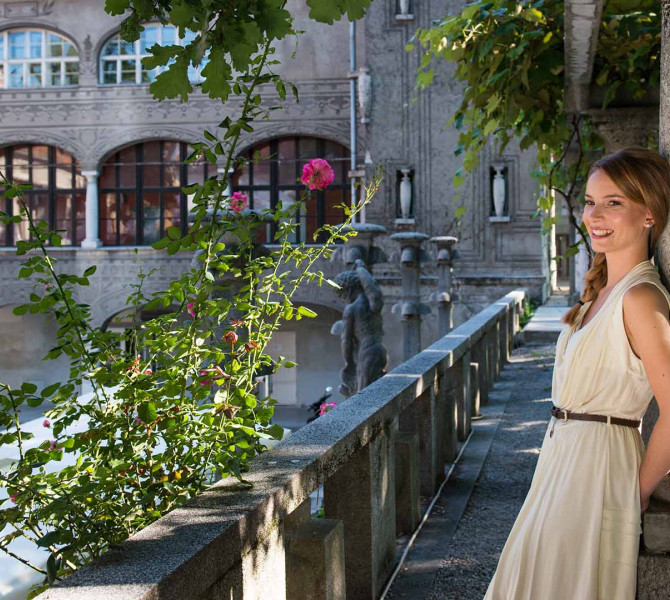 A girl leaning against a tree in Križanke. A building in the background.