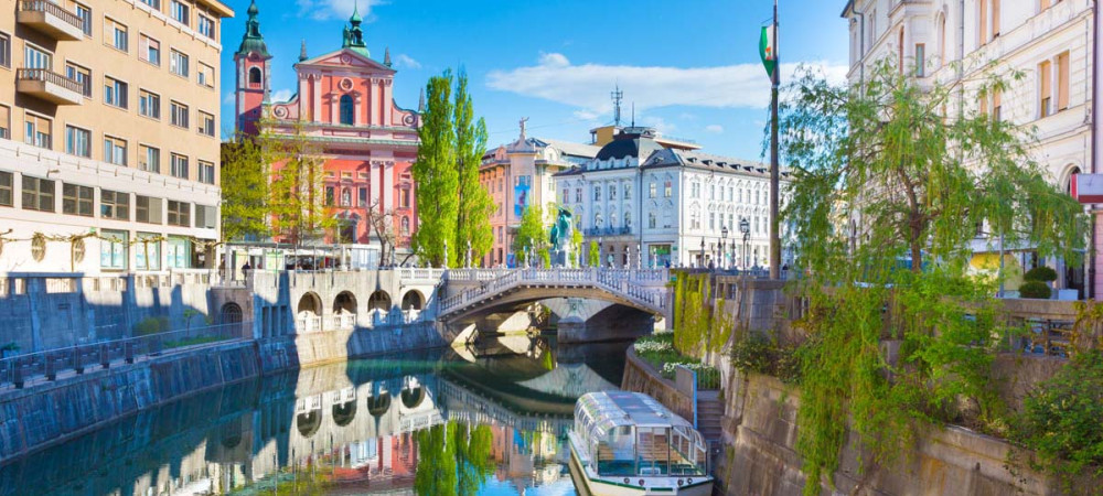 Razgled iz mostu na turistično ladjo na Ljubljanici. V ozadju Tromostovje in Prešernov trg.